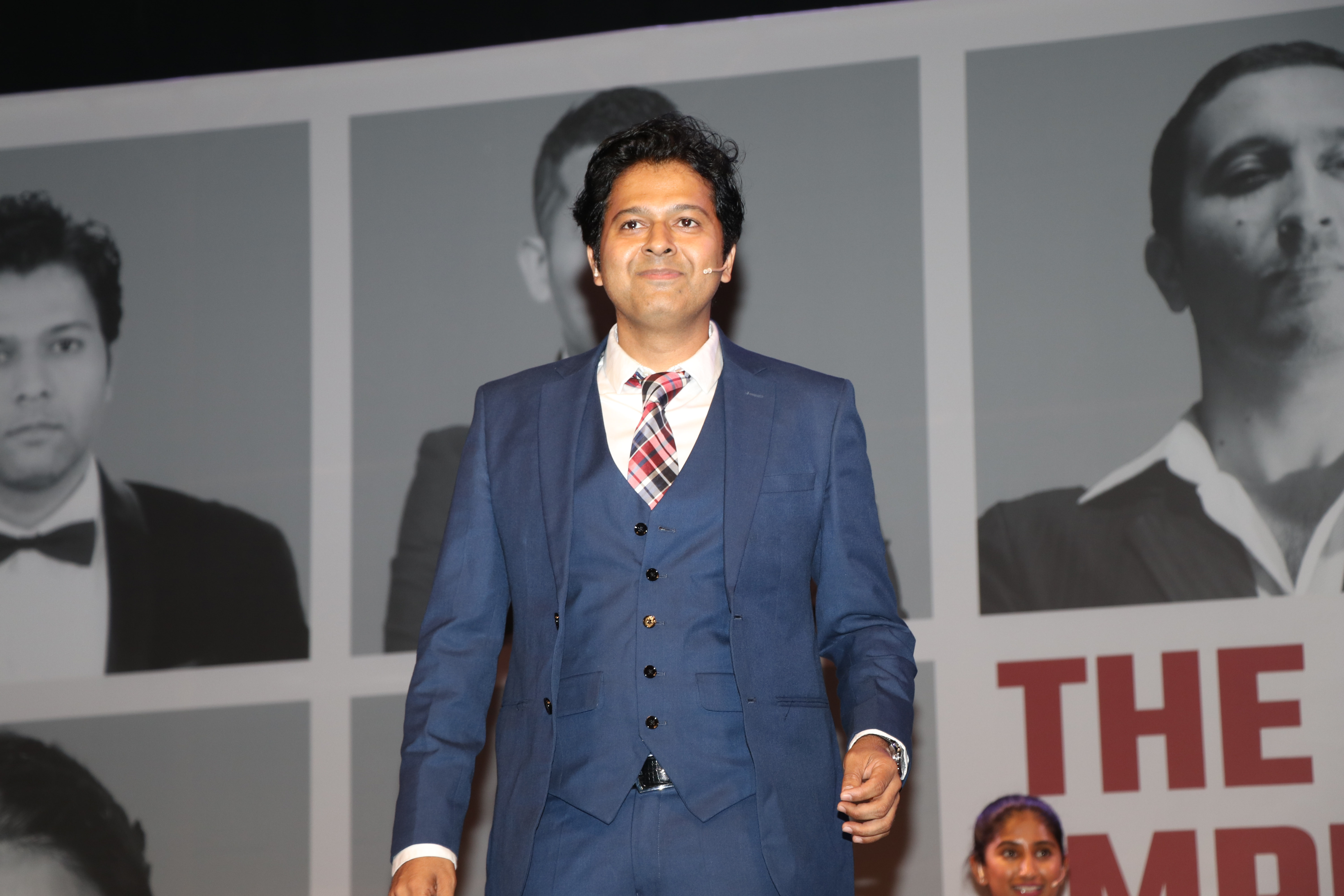 Saad Khan walking on stage in a blue three-piece suit